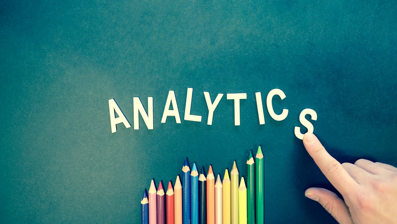 about-us Colored pencils and letters spelling 'ANALYTICS' on a textured background with a hand.