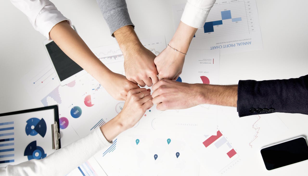 services-06 Colleagues celebrate success with a fist bump over financial charts depicting teamwork and unity.